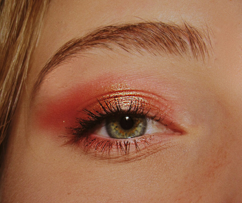 Ausschnitt eines grünen Auges mit rotem Lidschatten und Mascara