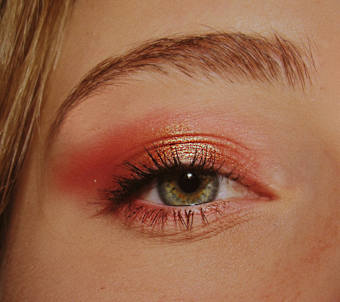 Ausschnitt eines grünen Auges mit rotem Lidschatten und Mascara